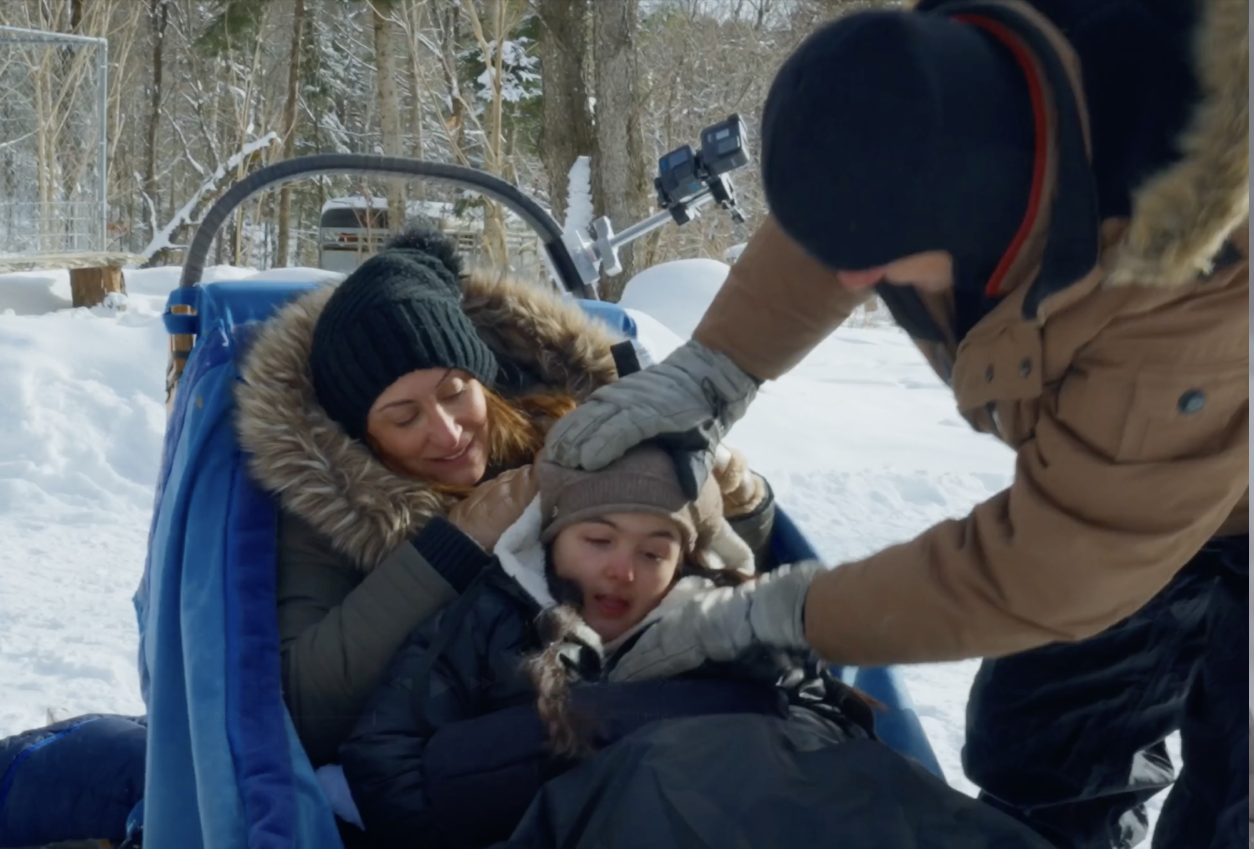 Caregiver helping a child into an adaptive dog sled before the ride