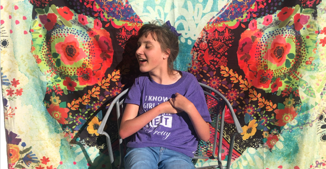 Lucy smiling, eyes closed, in front of a butterfly mural.
