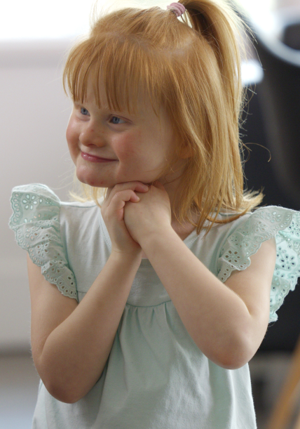 Minna smiling with her hands underneath her chin, looking away from camera.